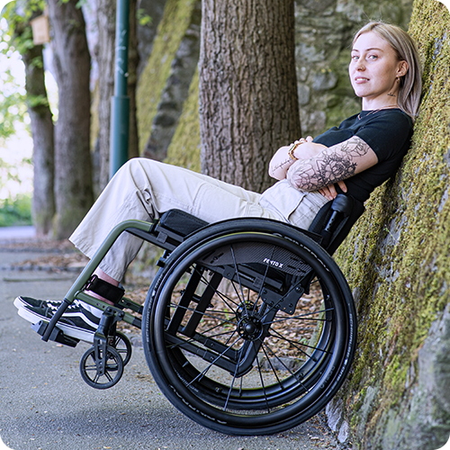 Una giovane donna appoggia la sua carrozzina a un muro di pietra.