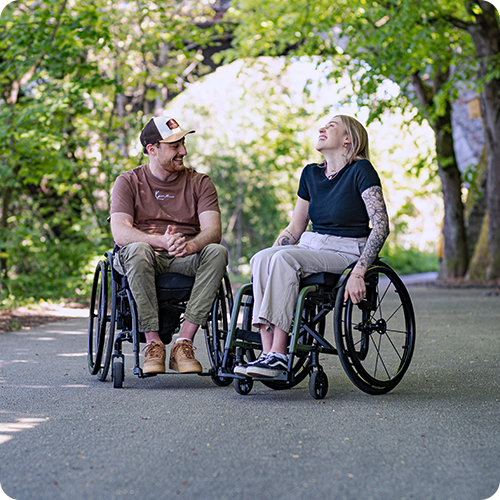 Una giovane donna e un giovanotto seduti su carrozzine si sorridono.
