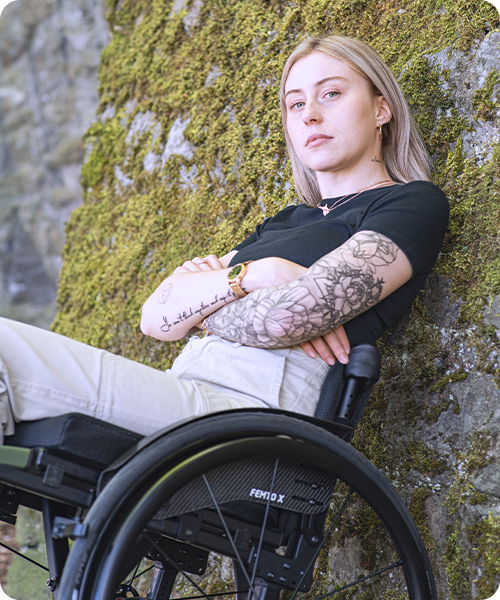 Una giovane donna è seduta nella sua carrozzina vicino a un muro di pietra.